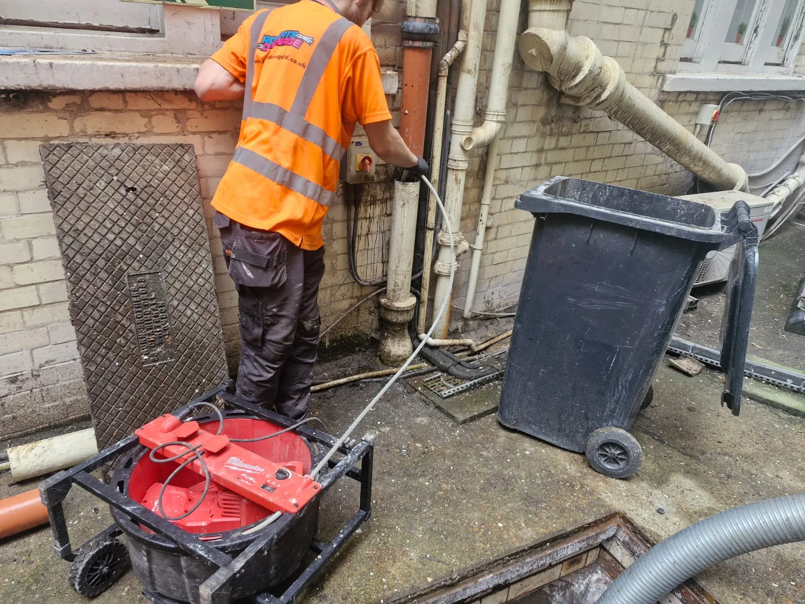 A professional drainage engineer from Roberts Drainage Ltd unblocking a pipe with a mechanical drain cleaner.