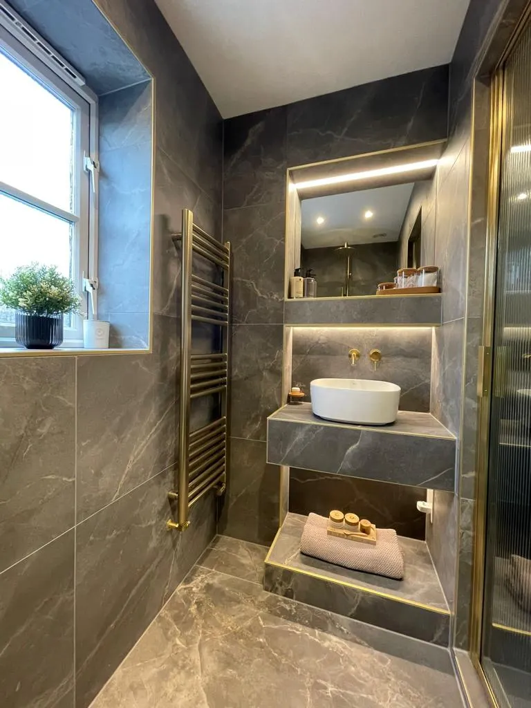 Luxury master bathroom installation in Plymouth featuring dark marble tiles, integrated LED lighting, and gold accents by Sands & Vossen.