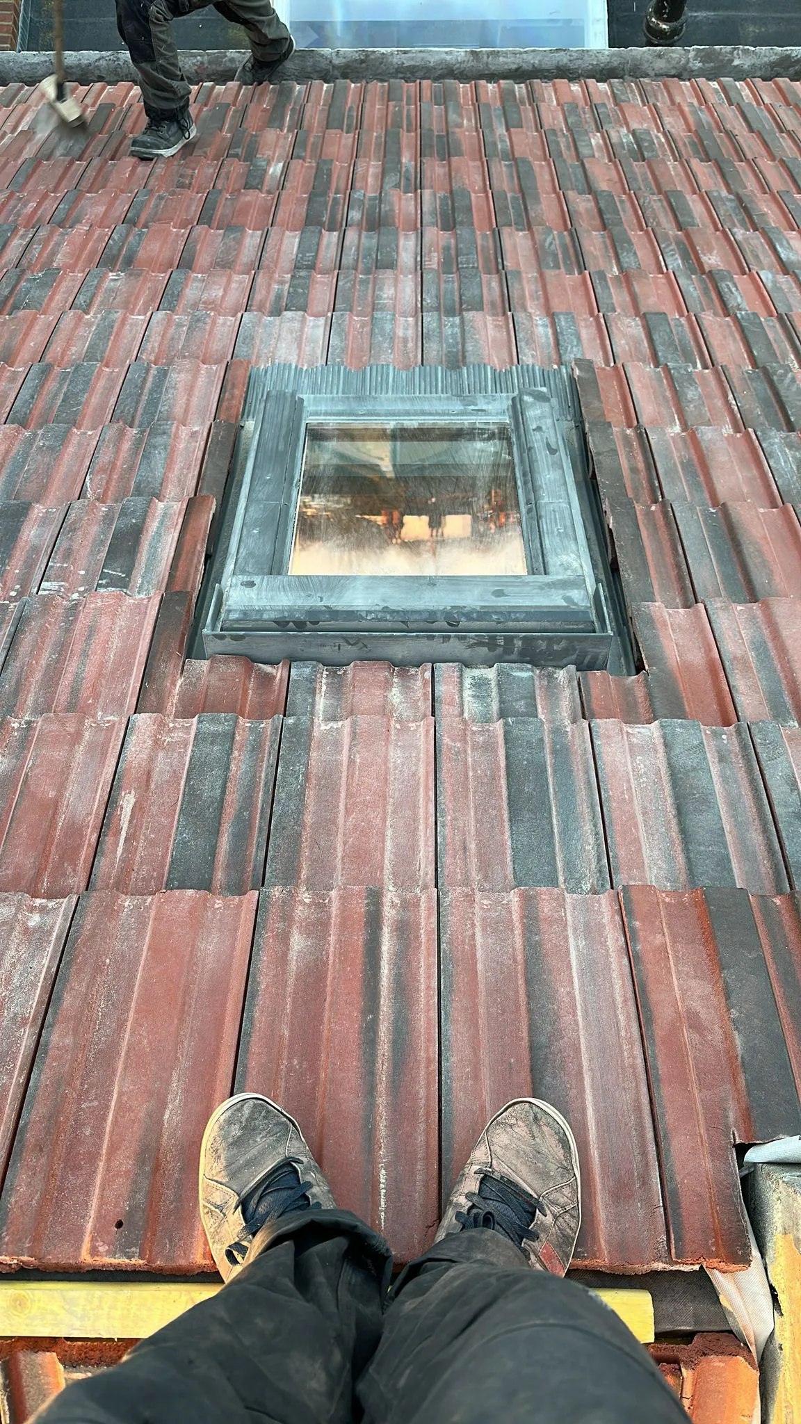 Concrete roof tiles laid neatly around a pitched roof skylight window with flashing