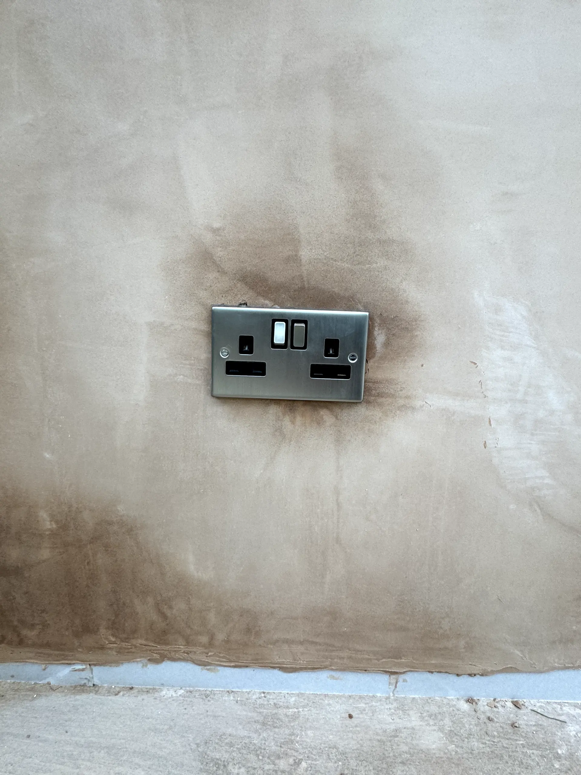 Newly installed brushed steel double socket with USB ports on freshly plastered wall