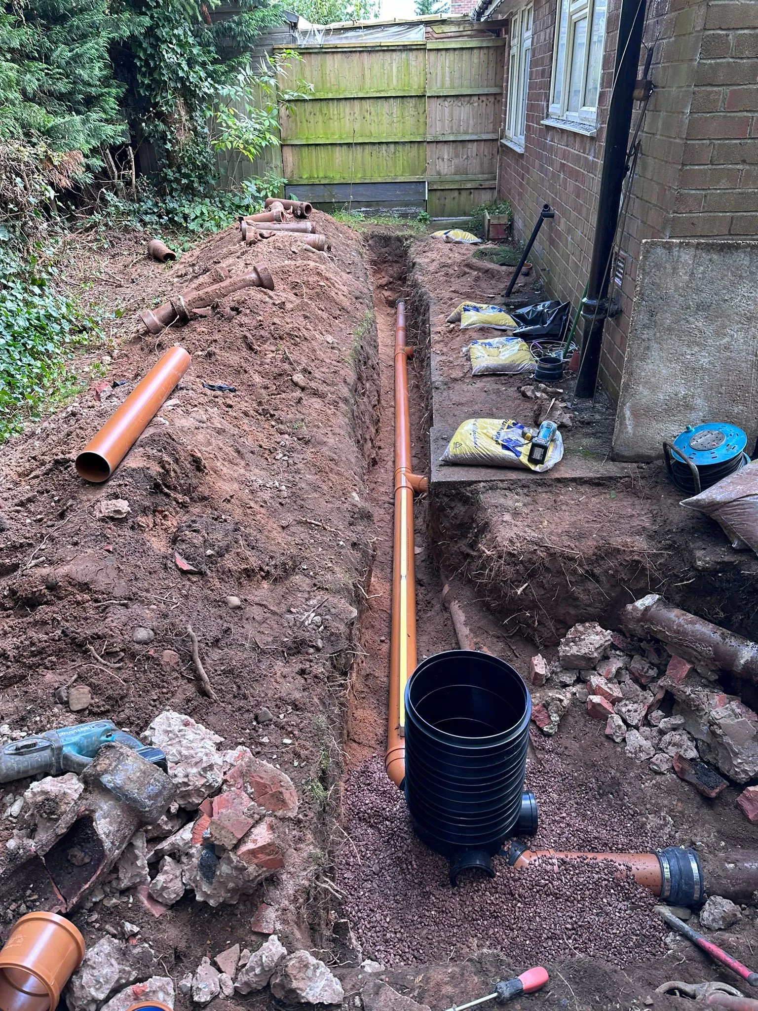 New drainage pipes and inspection chamber being installed in an excavated trench at a residential property.