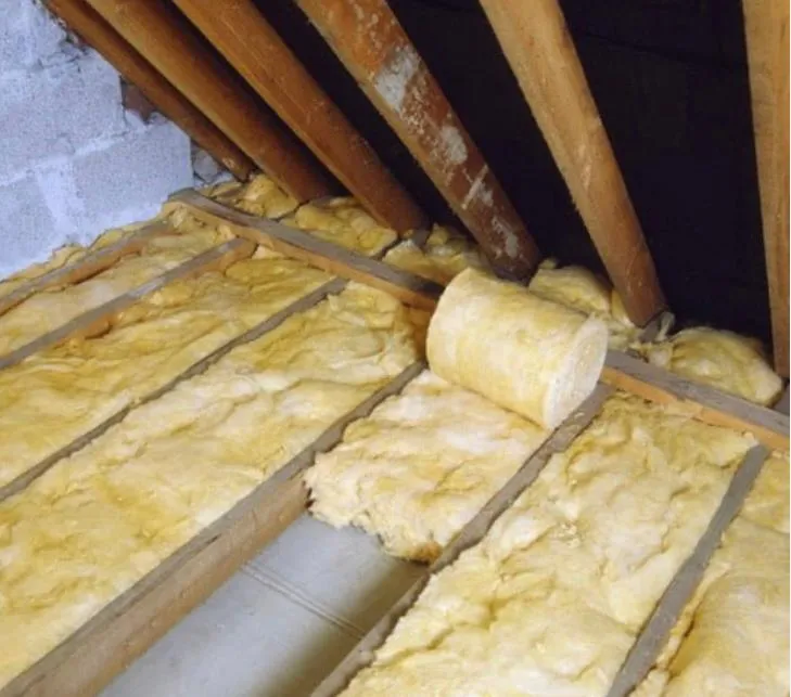 Mineral wool loft insulation being installed between wooden attic joists.