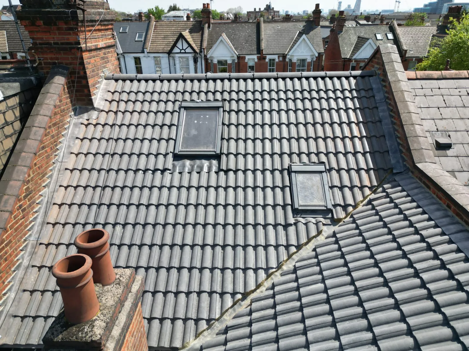 Grey tiled pitched roof with skylights and chimney.
