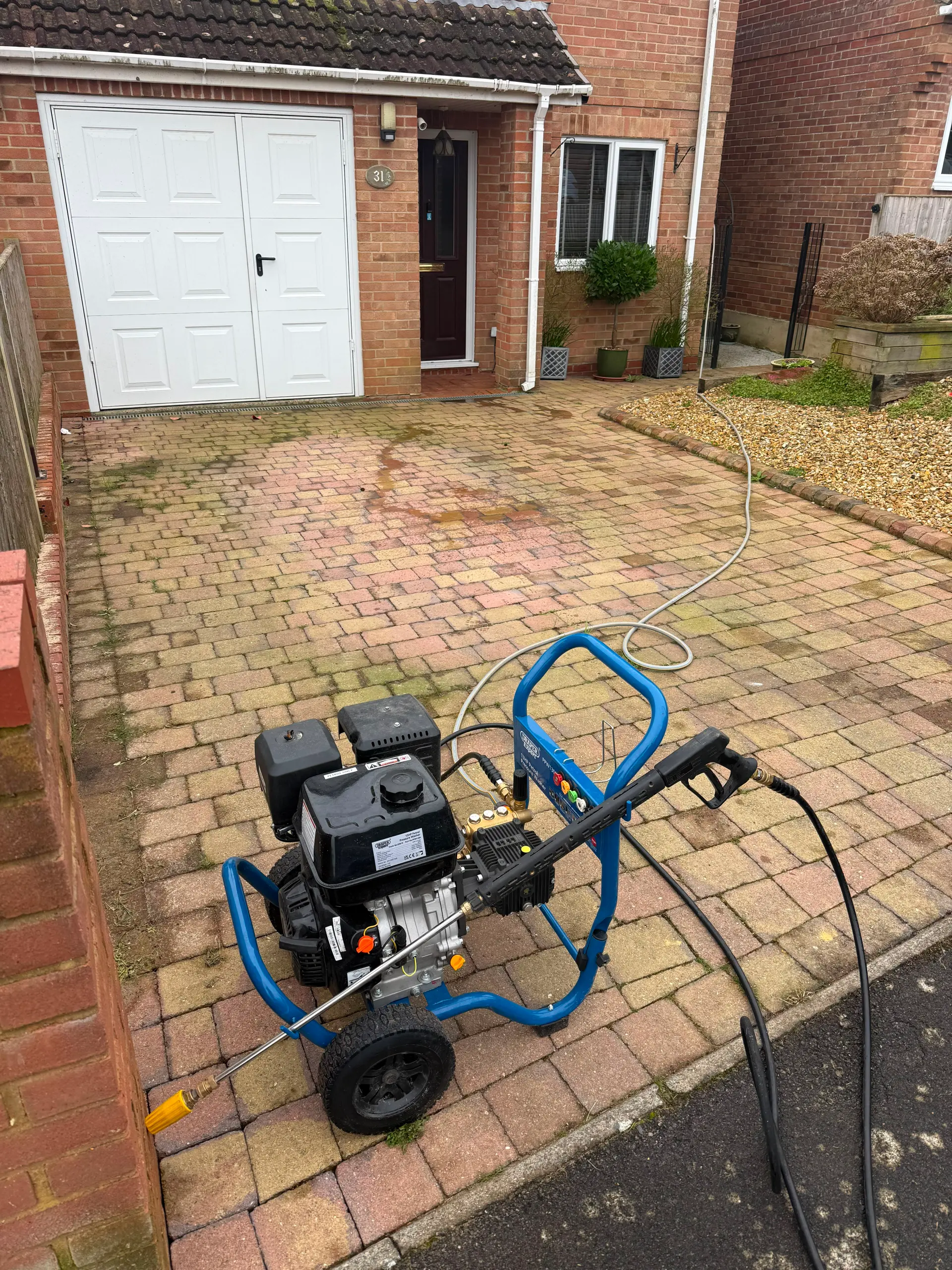 A professional pressure washer machine sitting on a block-paved driveway outside a residential property