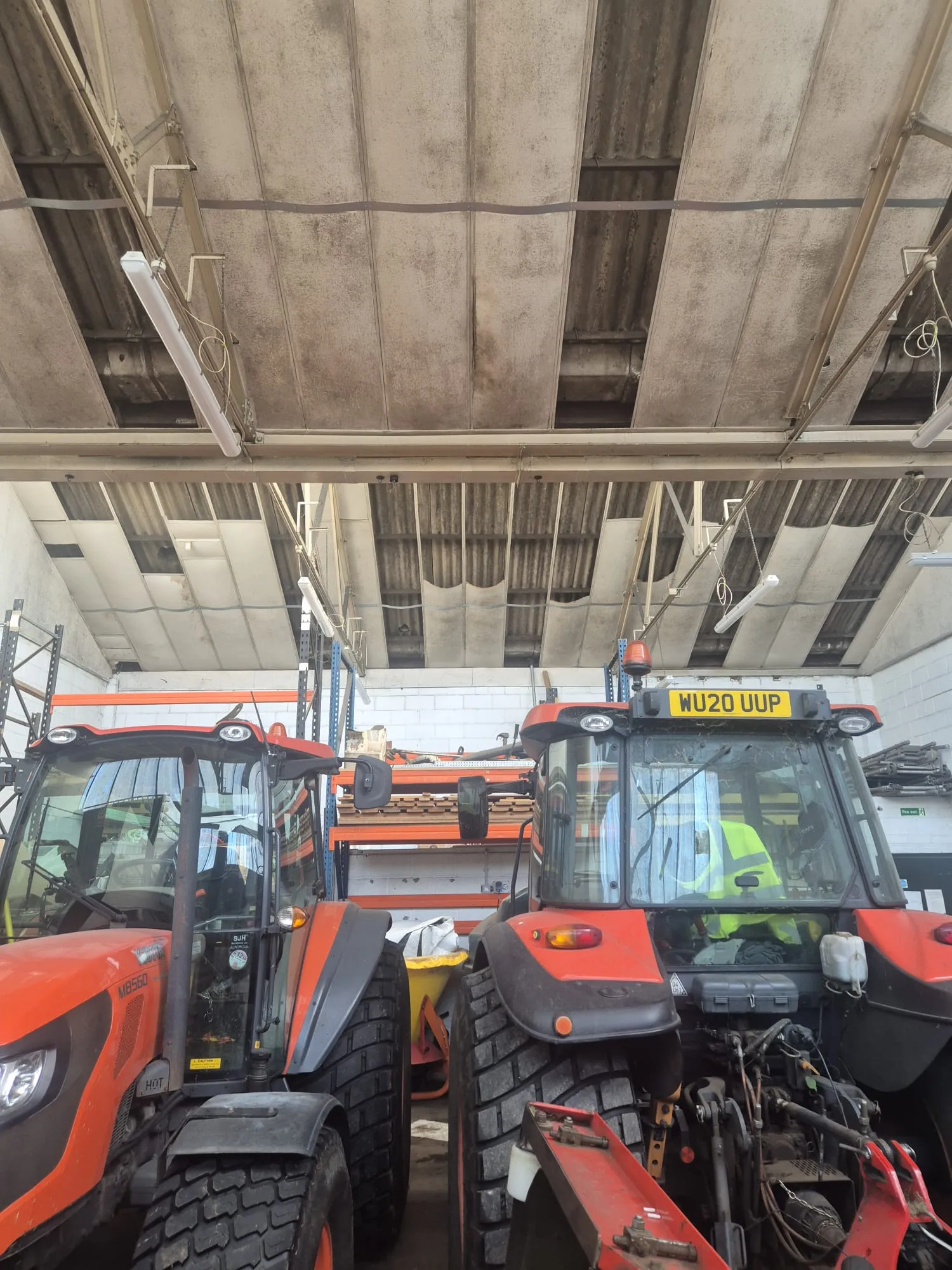 Two large red agricultural tractors parked inside a commercial warehouse or workshop with an industrial roof and shelving.