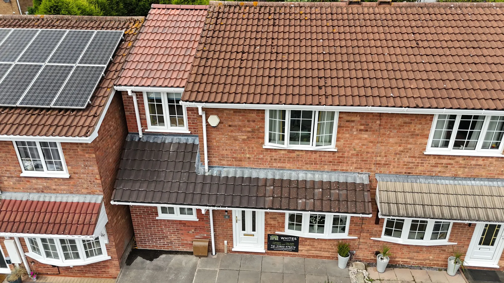 Aerial view of residential homes with varied rooflines, an extension, solar panels, and a Whites Building LTD sign.