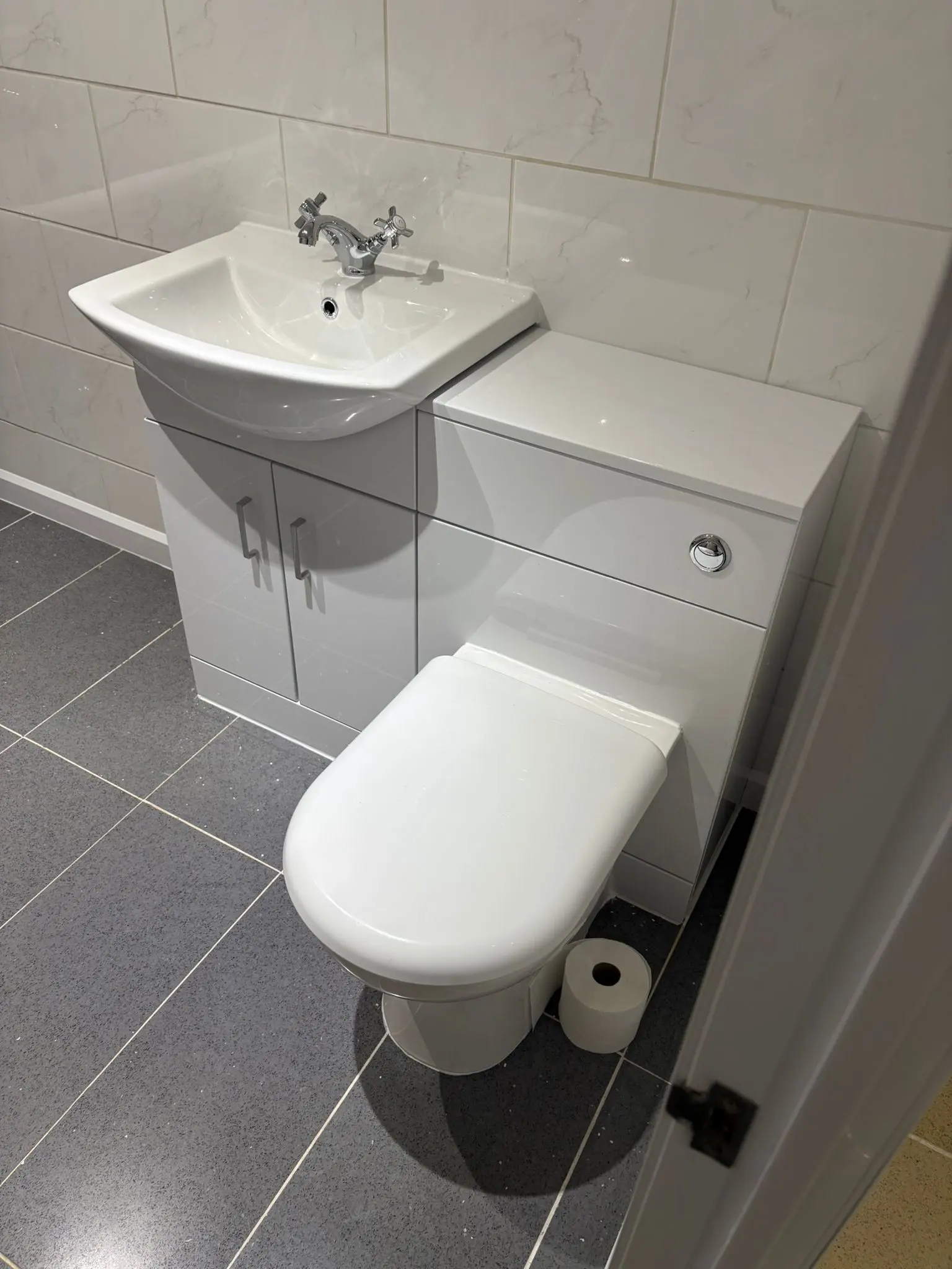 Modern bathroom refurbishment in Wolverhampton featuring integrated toilet and basin vanity unit with high-gloss tiling.