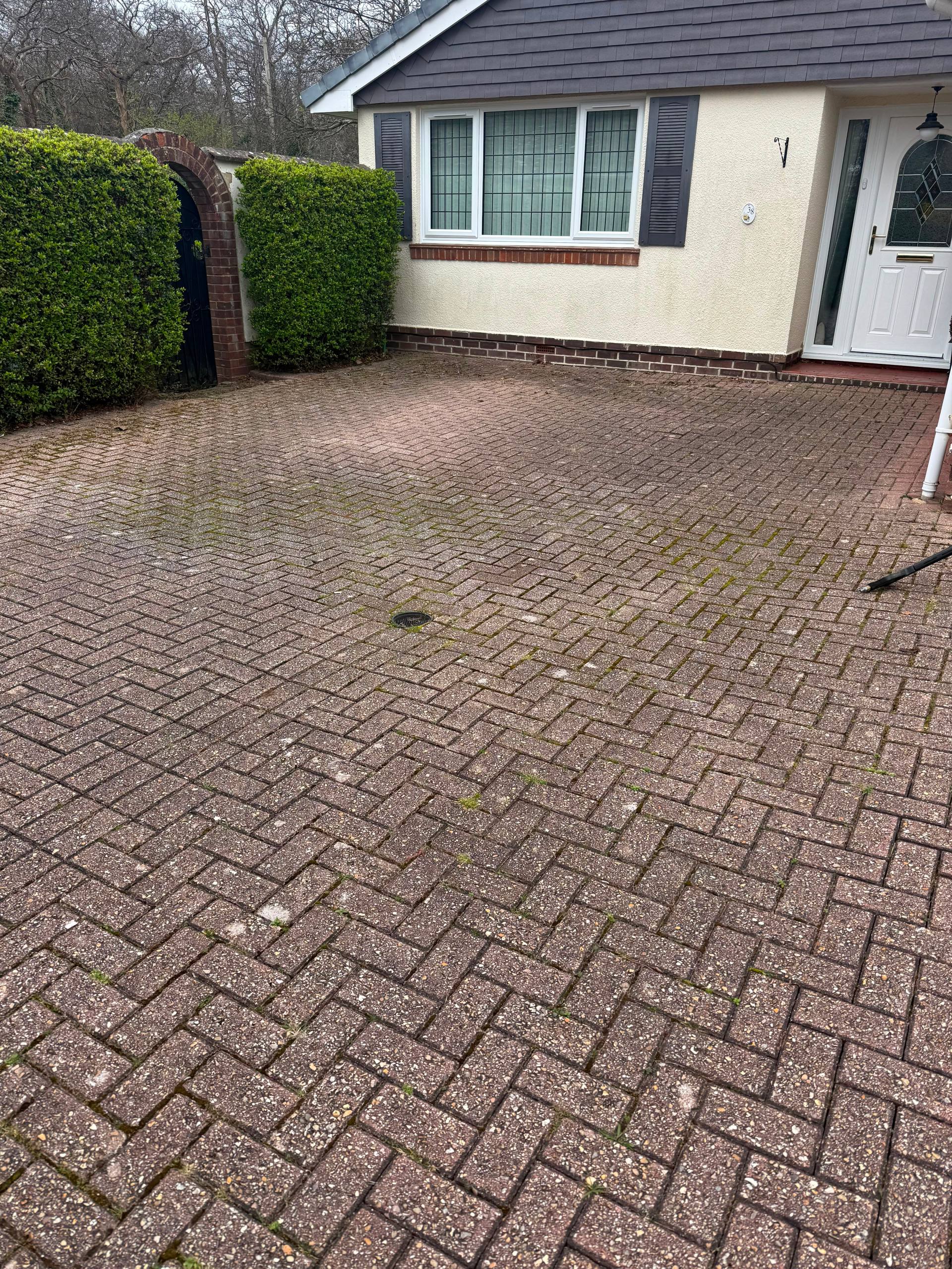 A dirty block paving driveway with moss and weeds requiring professional pressure washing and re-sanding