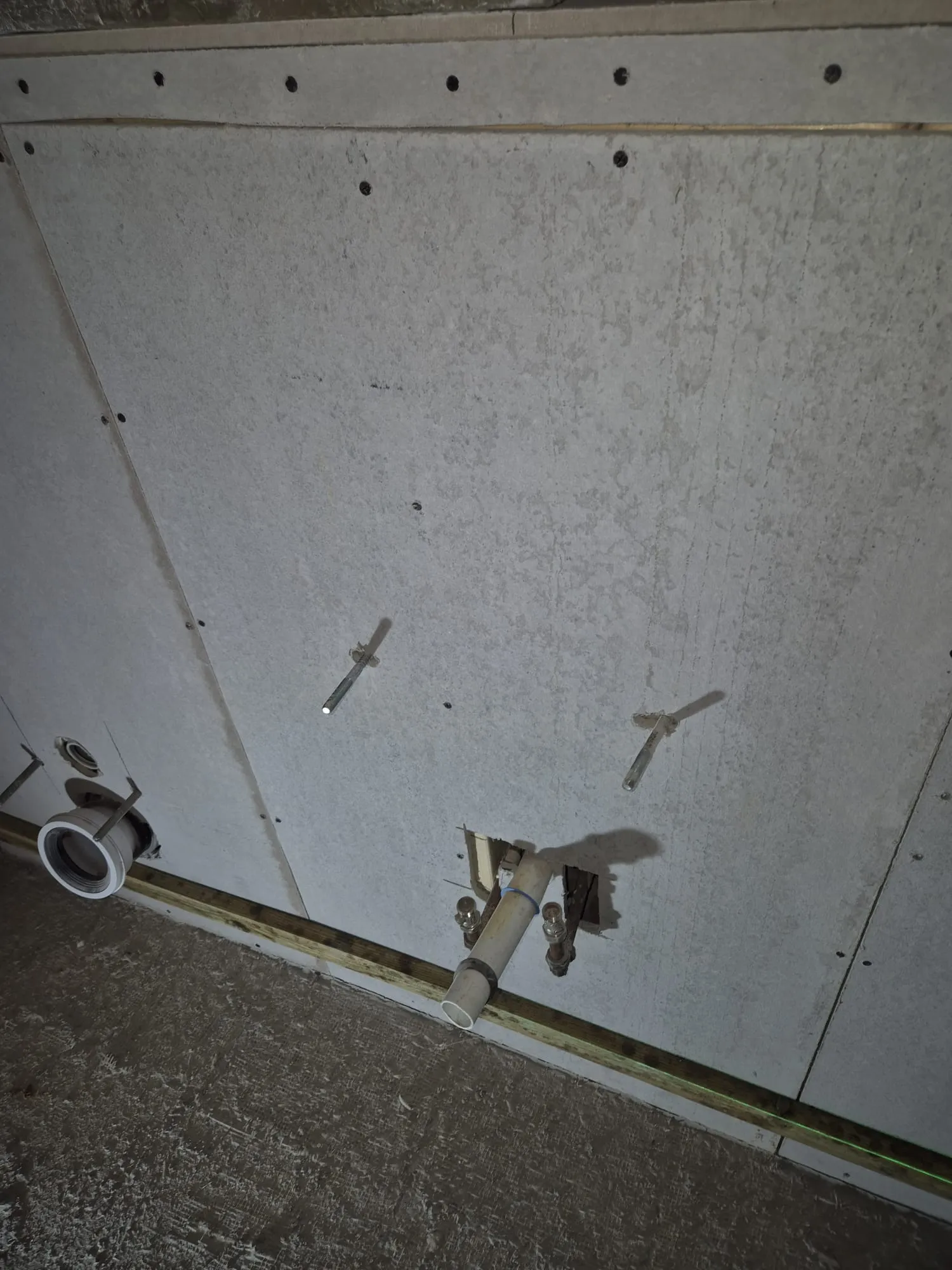 An unfinished internal wall with new plasterboard, plumbing pipes, and fixture supports visible during a home renovation.