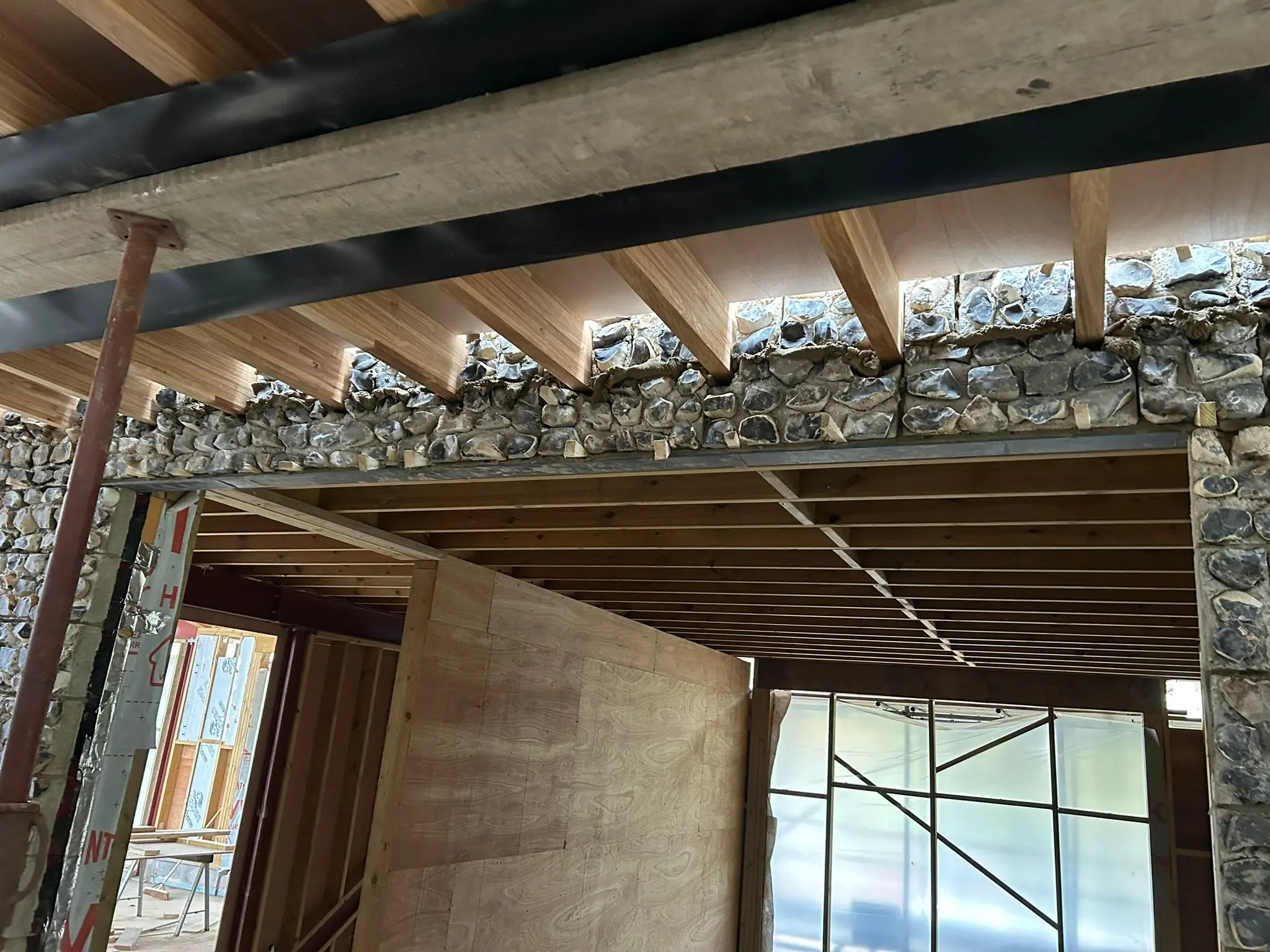 Structural steel RSJ installation and new timber joists fitted onto a traditional flint stone wall during a property renovation.