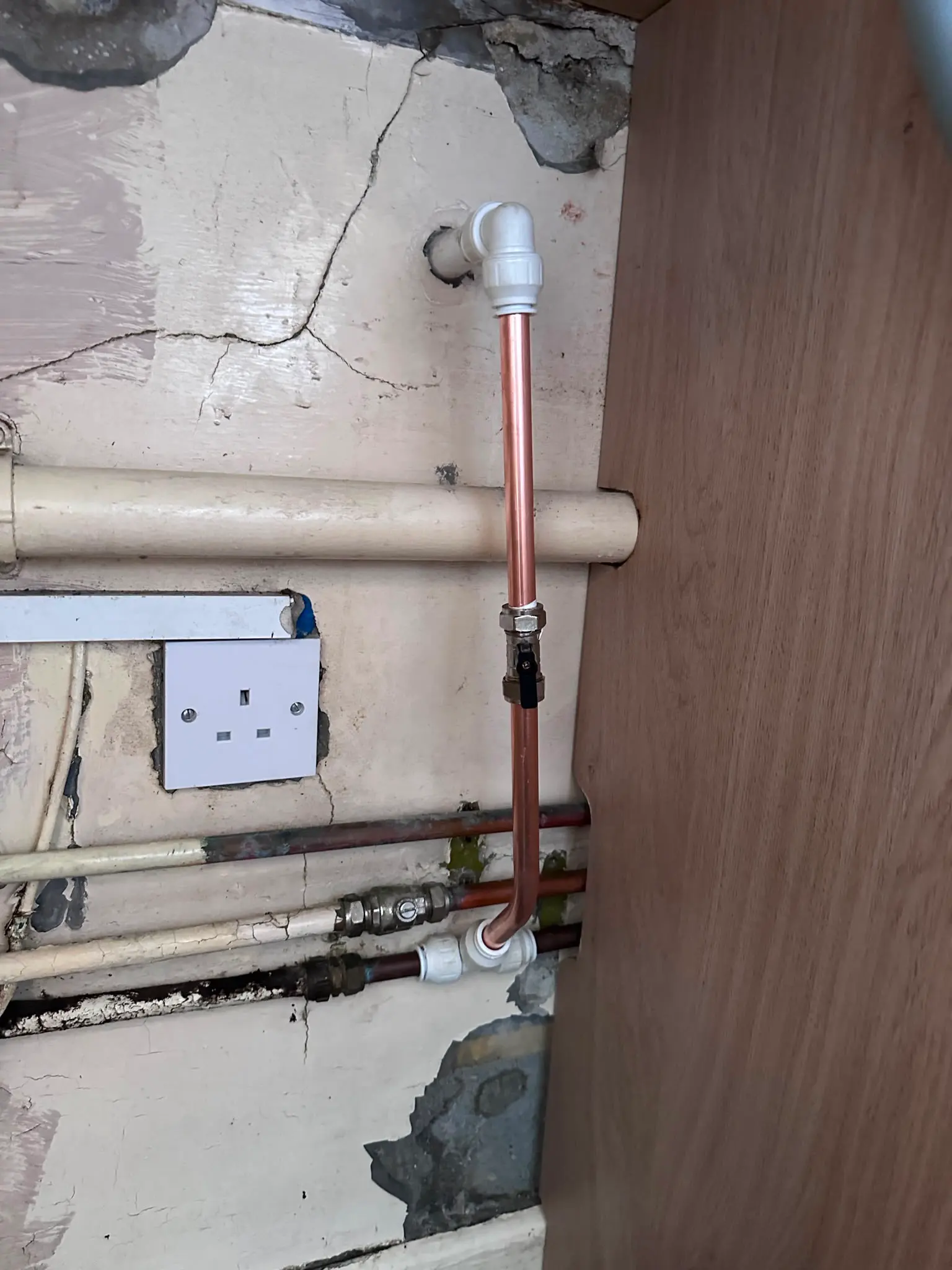 Close up of new copper plumbing pipework and an isolation valve connected to older pipes next to an electrical socket.