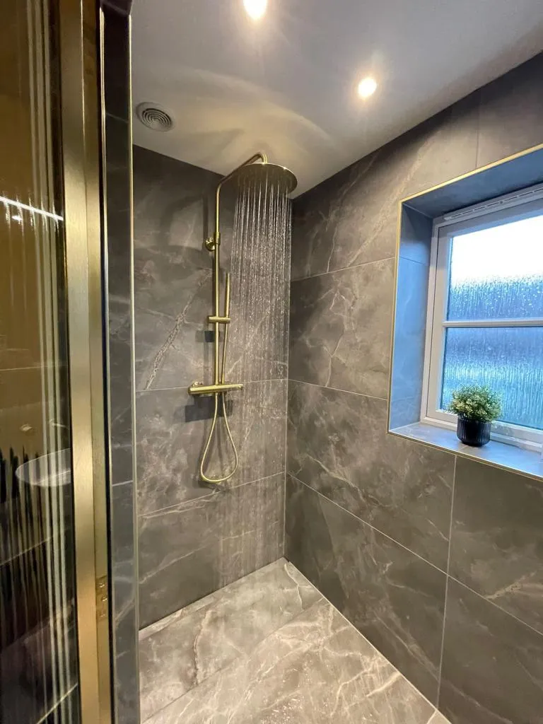 Bespoke walk-in shower installation with marble-effect tiling and gold fittings by Sands & Vossen in Plymouth.