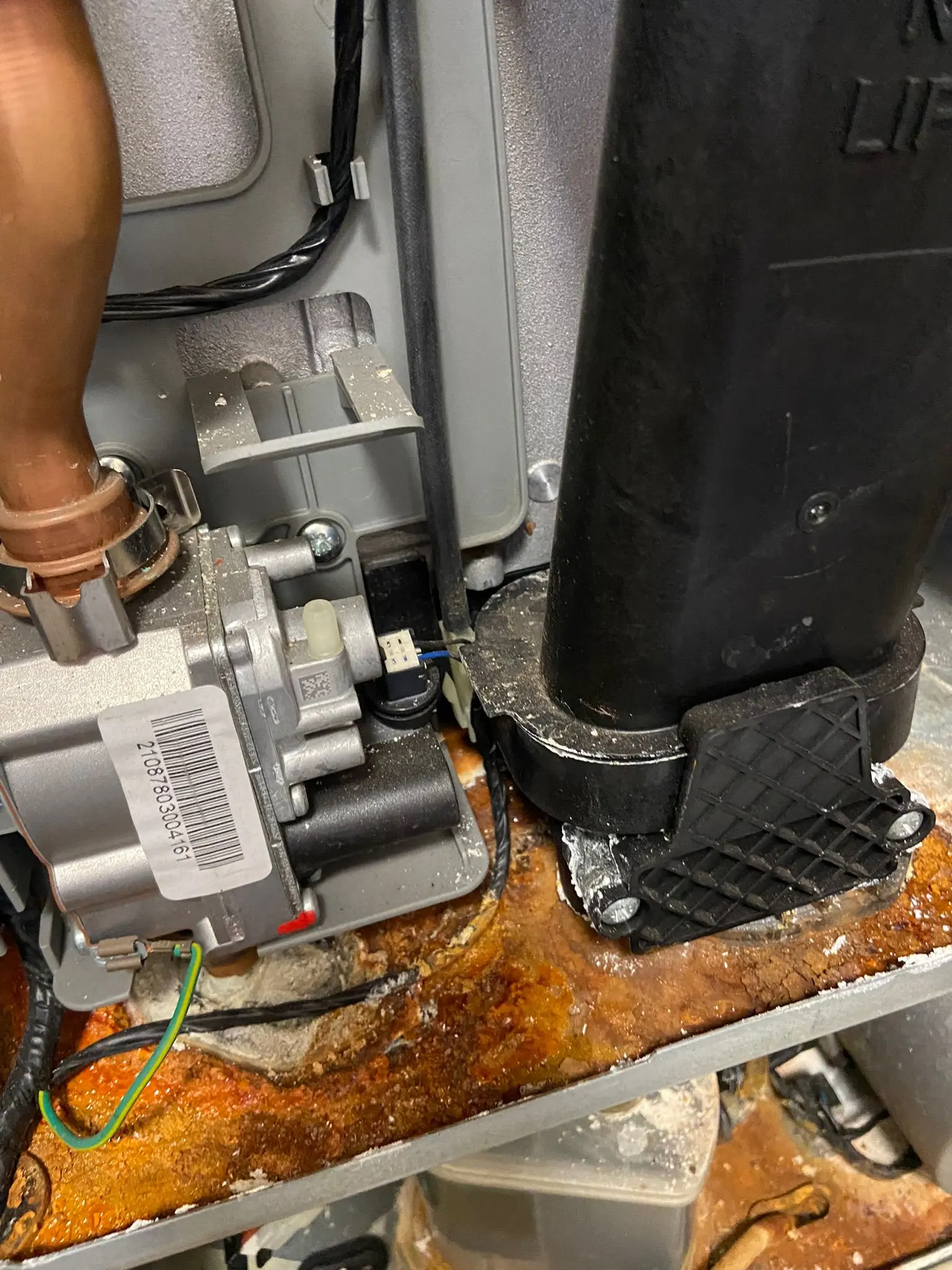 Internal components of a leaking gas boiler with significant rust and corrosion requiring emergency repair.