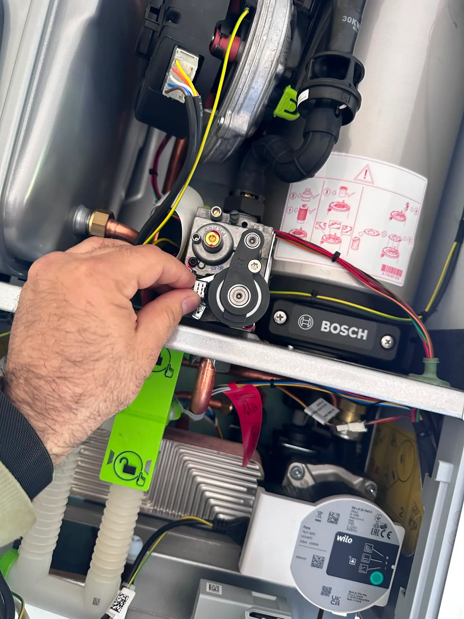 A close up of a person's hand adjusting a component inside a Bosch boiler