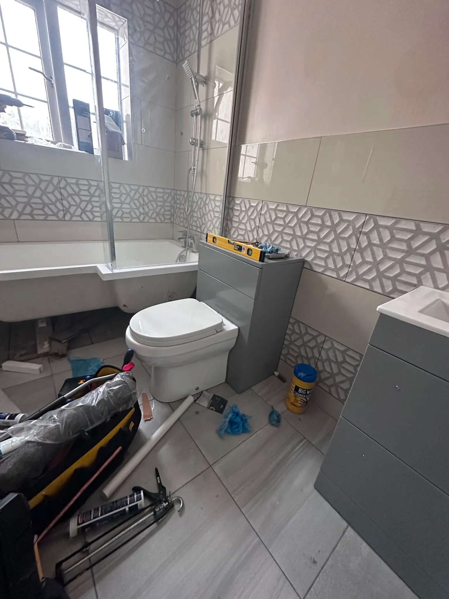 A bathroom undergoing refurbishment, showing a new bath, toilet, and vanity unit being installed, with tools scattered on the floor.