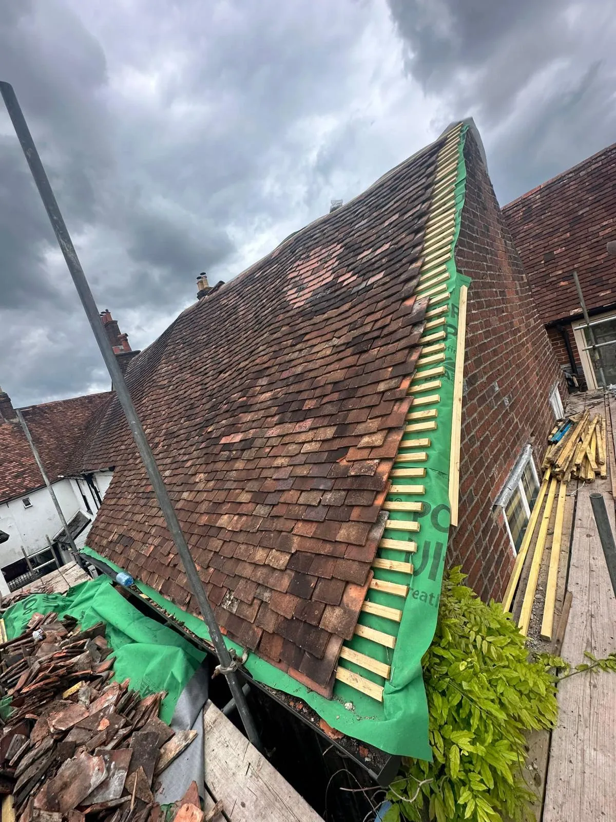 Tiled roof in the process of re-roofing, showing old tiles next to new green underlay and wooden battens.