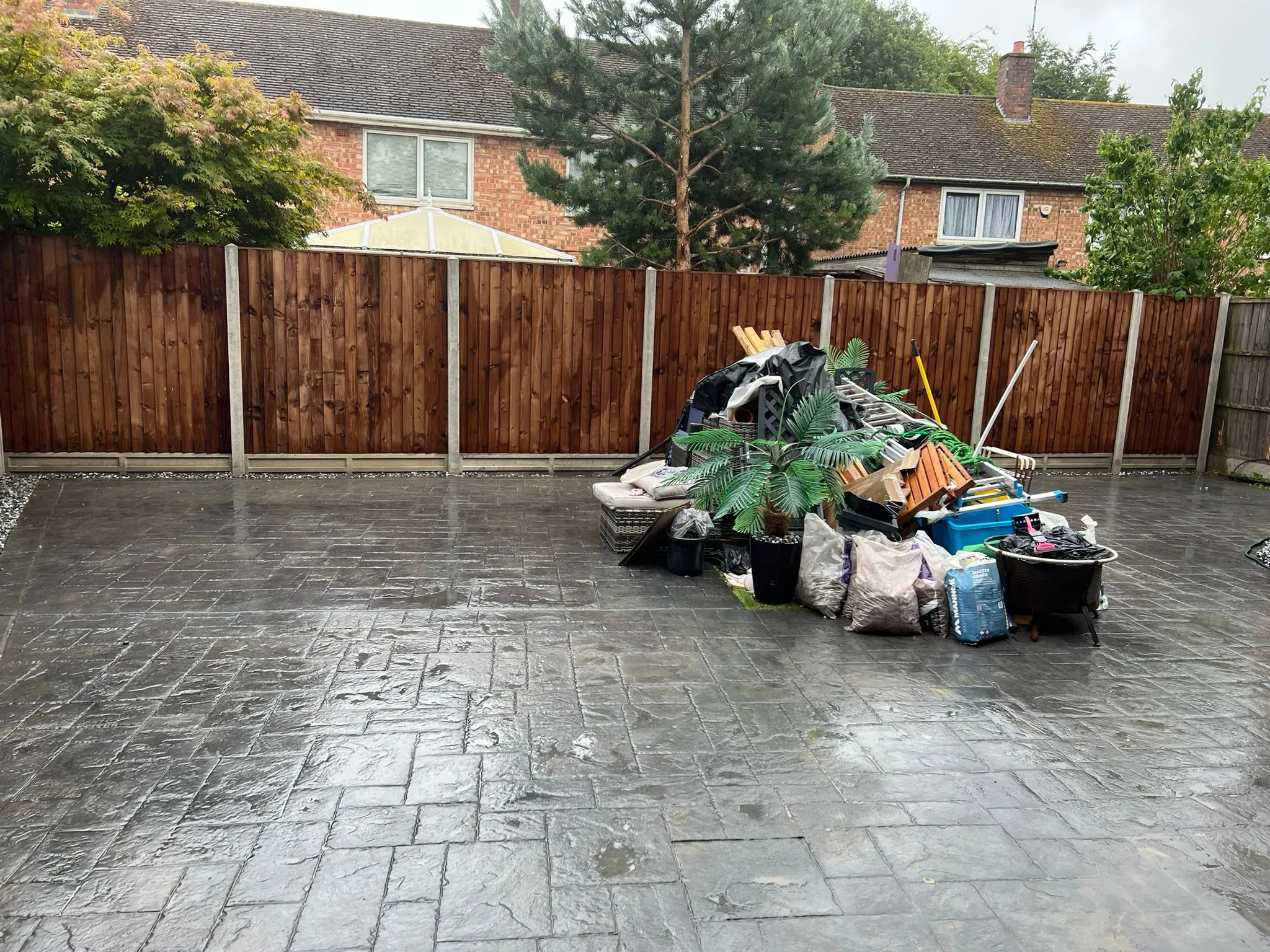 Newly installed dark wooden closeboard fence and patterned grey paving, with garden waste awaiting removal.