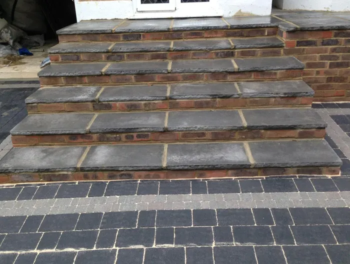 Close-up of recently built outdoor steps with brick risers and natural stone treads, next to a pattern-laid block paving driveway or patio.