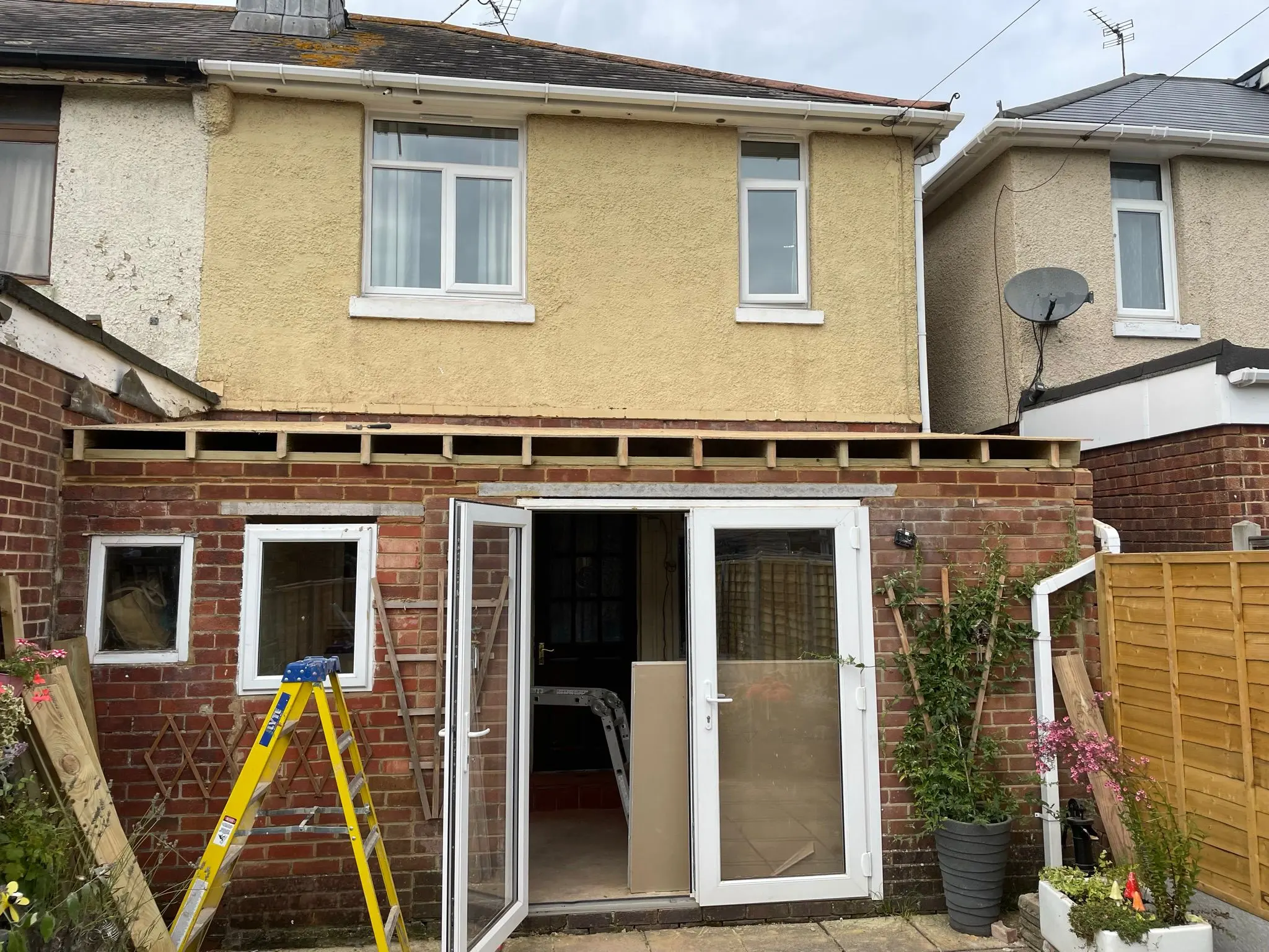 Single-storey brick house extension under construction with exposed roof joists and French doors