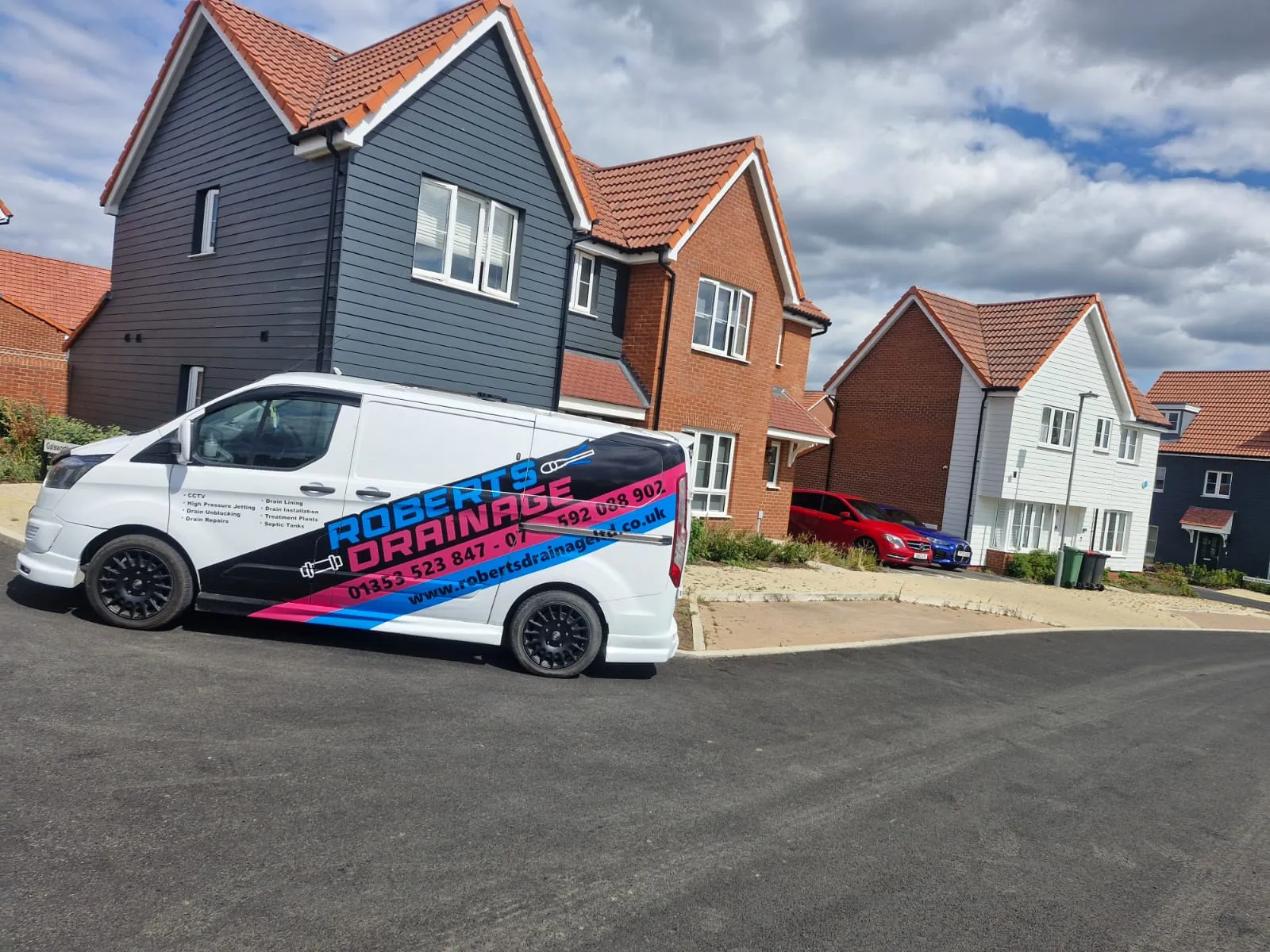 A white Roberts Drainage Ltd service van parked outside a row of modern houses in a residential area of Cambridgeshire.