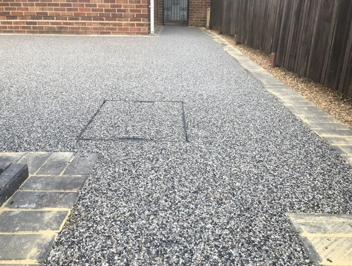 Newly laid grey resin-bound driveway with an integrated drain cover and block paving border, leading to a house entrance.