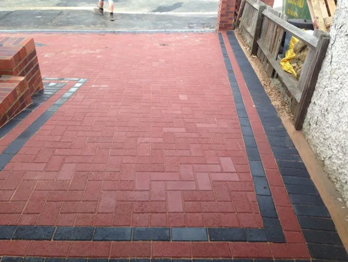 A newly installed red and black block paved driveway with a herringbone pattern, bordered by black paving, next to a brick step.