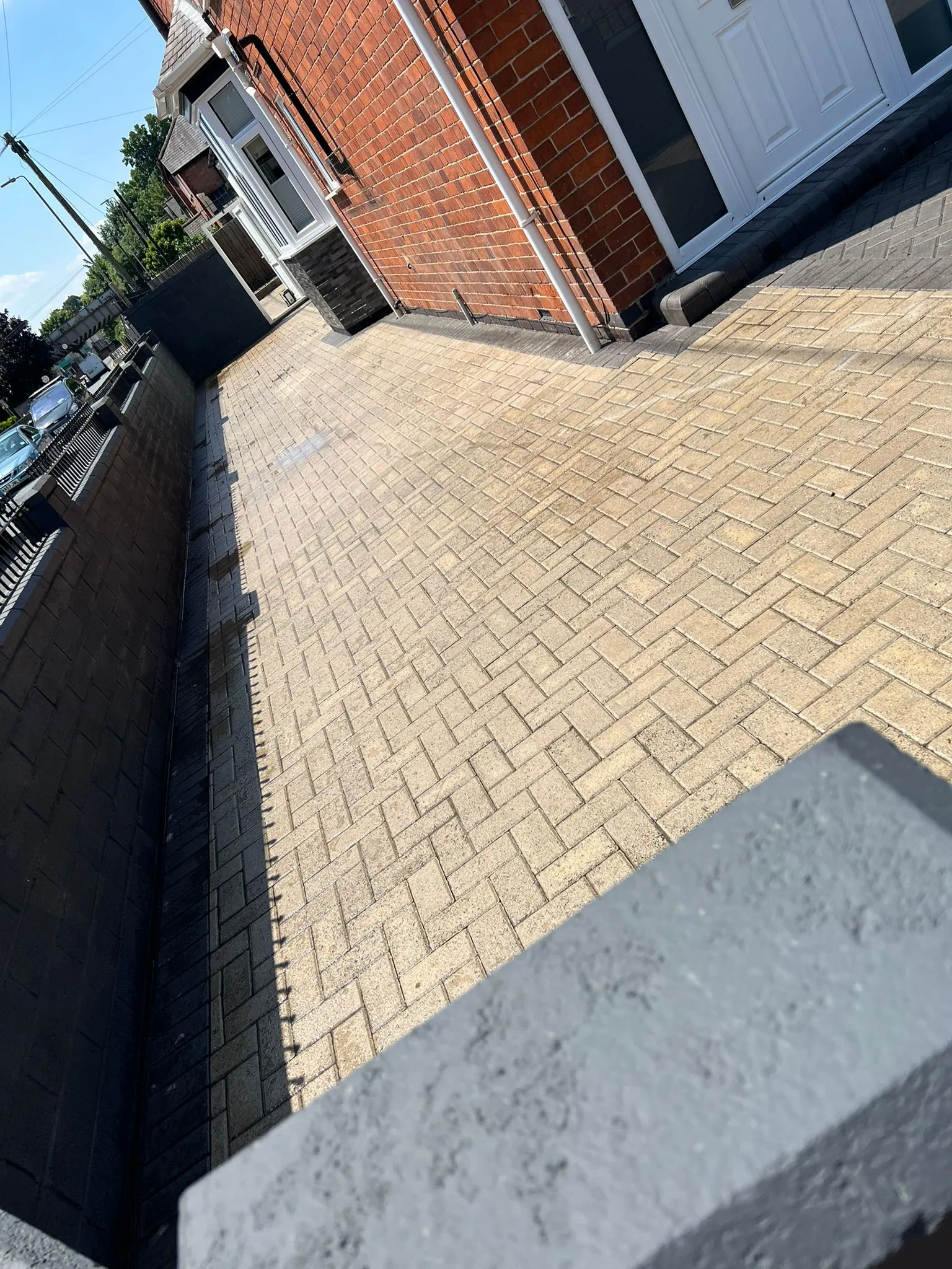 Newly laid block paving driveway with light-coloured bricks and a dark grey garden wall next to a house.