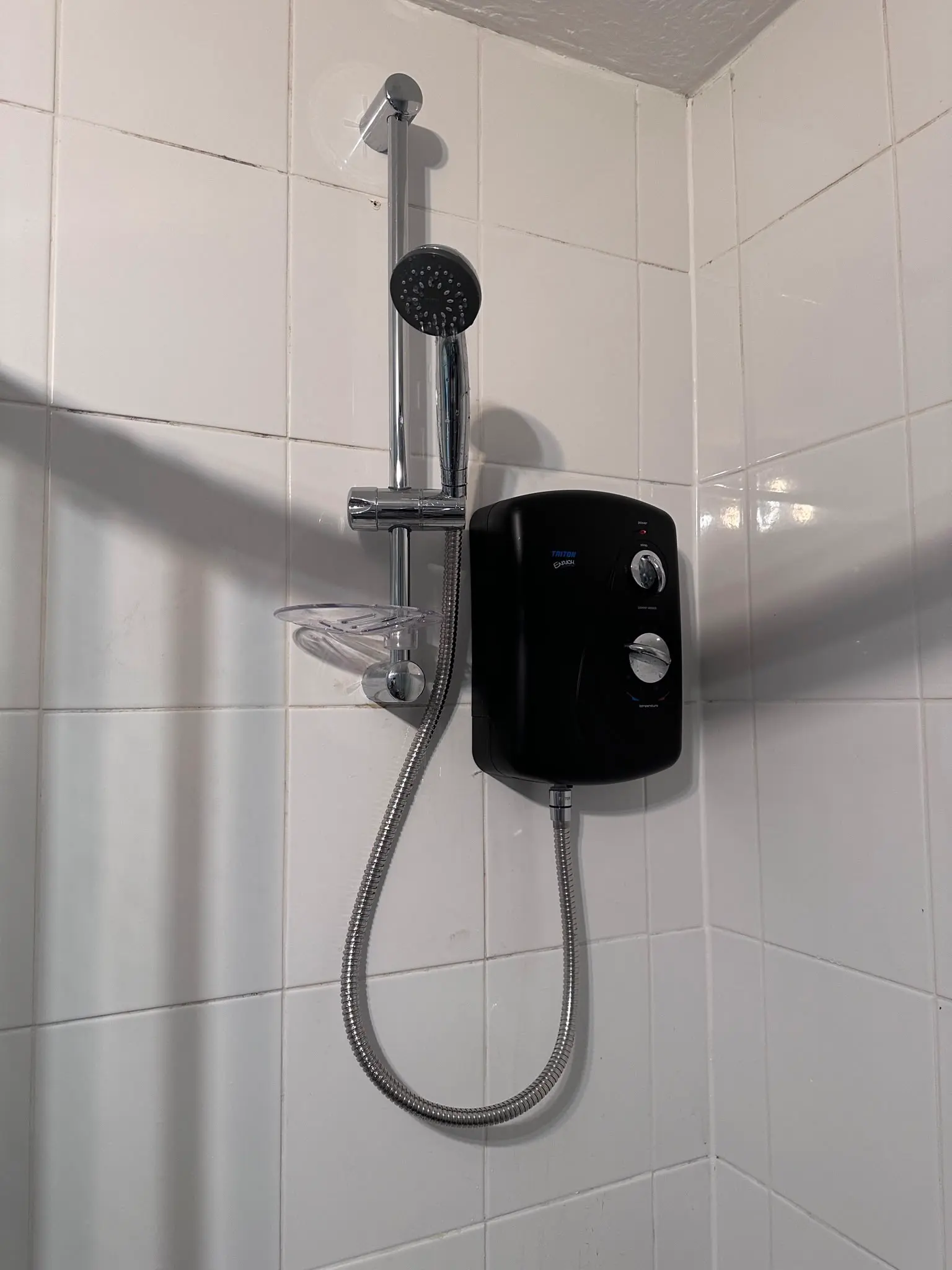 Black electric shower and chrome riser rail installed on white tiles by JMA Plumbing & Heating in Snodland