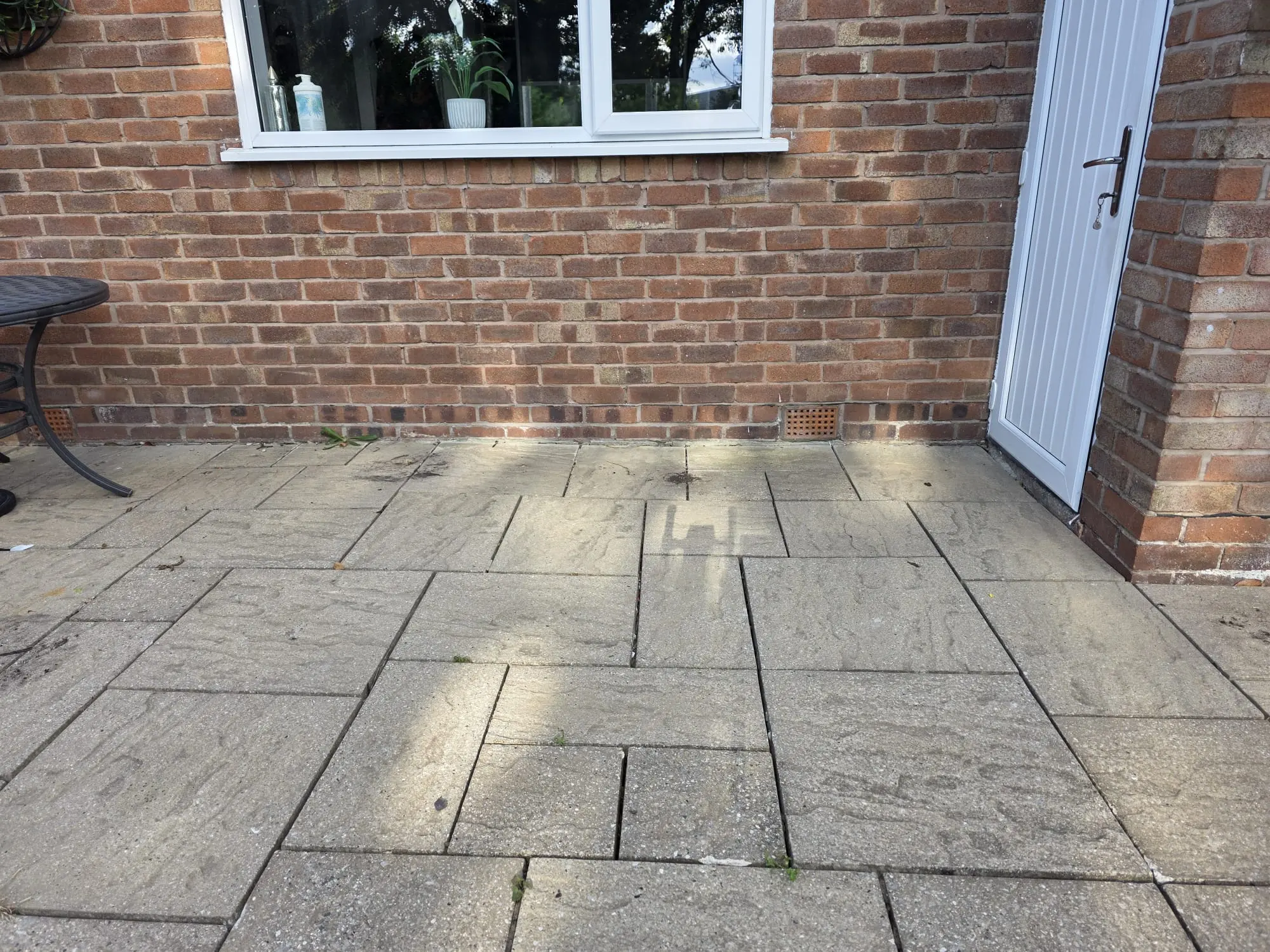 Recessed inspection chamber cover on a paved patio next to a brick house