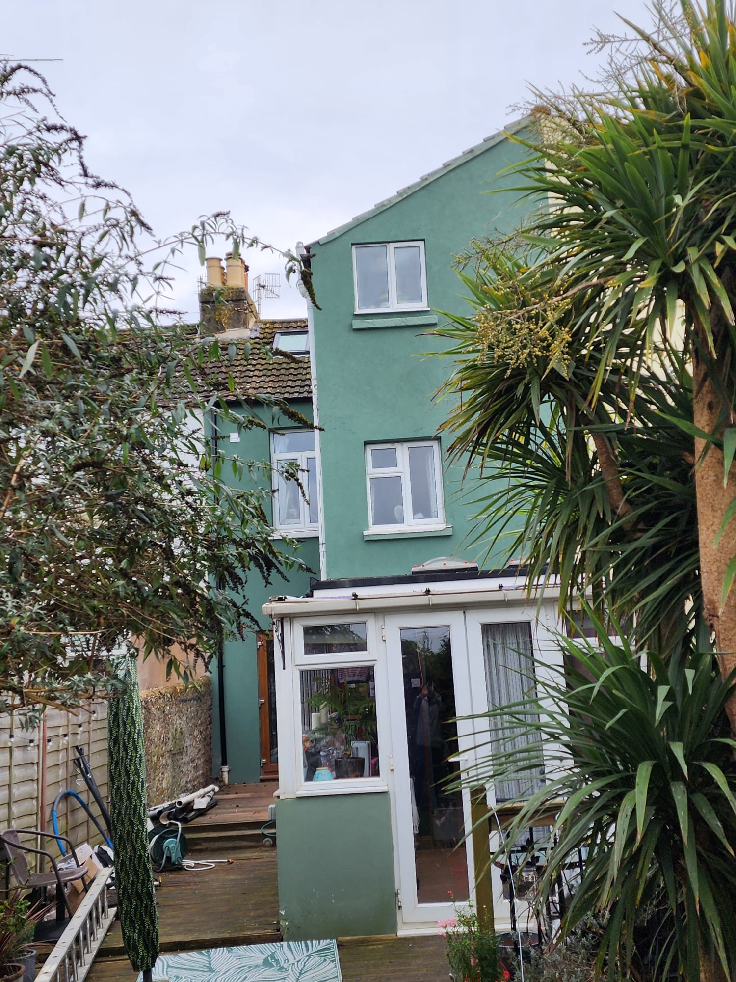 A house with fresh green external rendering and a white conservatory in a garden setting