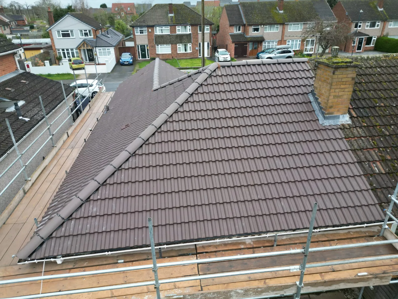 New brown tiled roof section installed during a re-roofing project, beside an older, mossy roof, demonstrating Rooflex Roofing's new roof services.