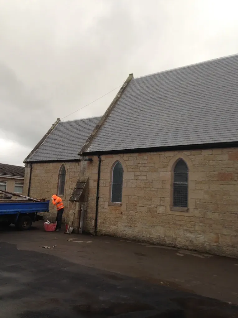 A large traditional building in Lanark featuring a newly installed or repaired slate roof with a tradesman and vehicle on site.