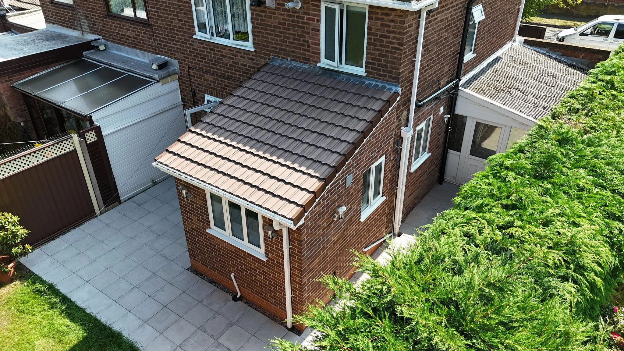 Aerial view of a modern single-storey home extension with brick walls and a brown tiled roof, alongside a paved patio and garden.