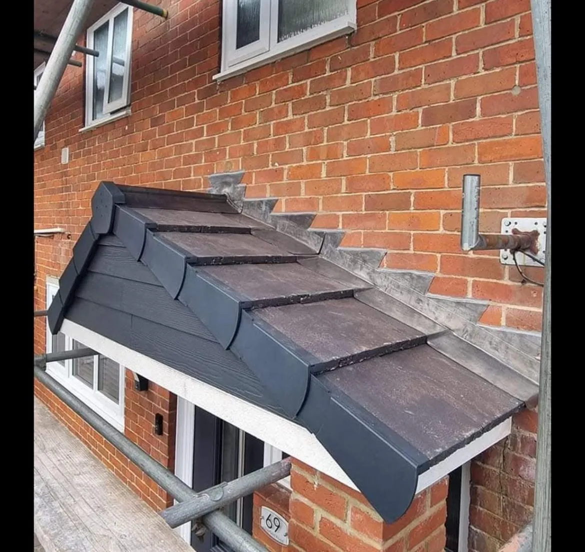 A newly installed pitched tiled porch roof with lead flashing and dark grey verge trim on a brick house.