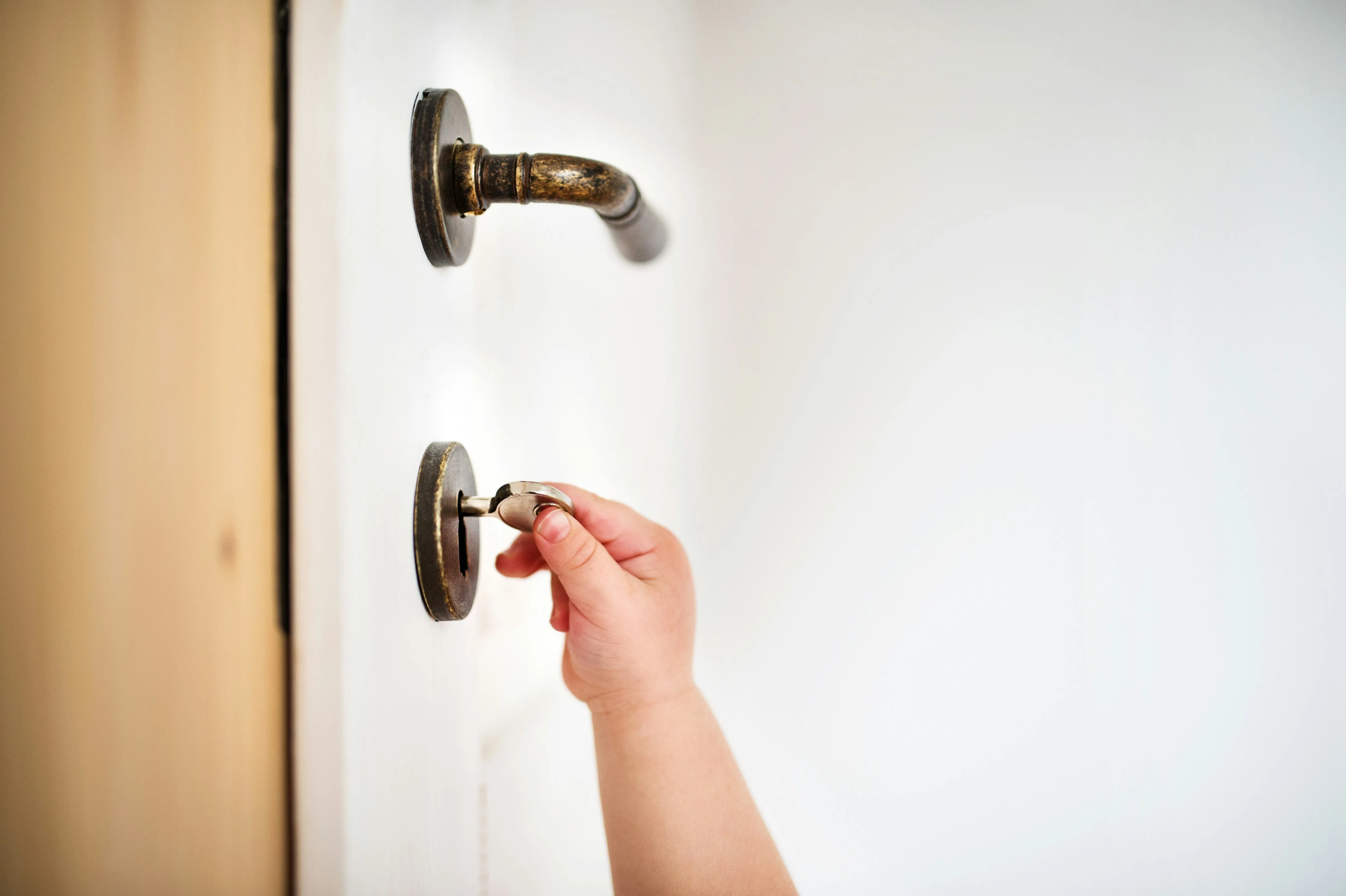 A close-up of a child's hand holding a key and trying to use an old-fashioned door lock.