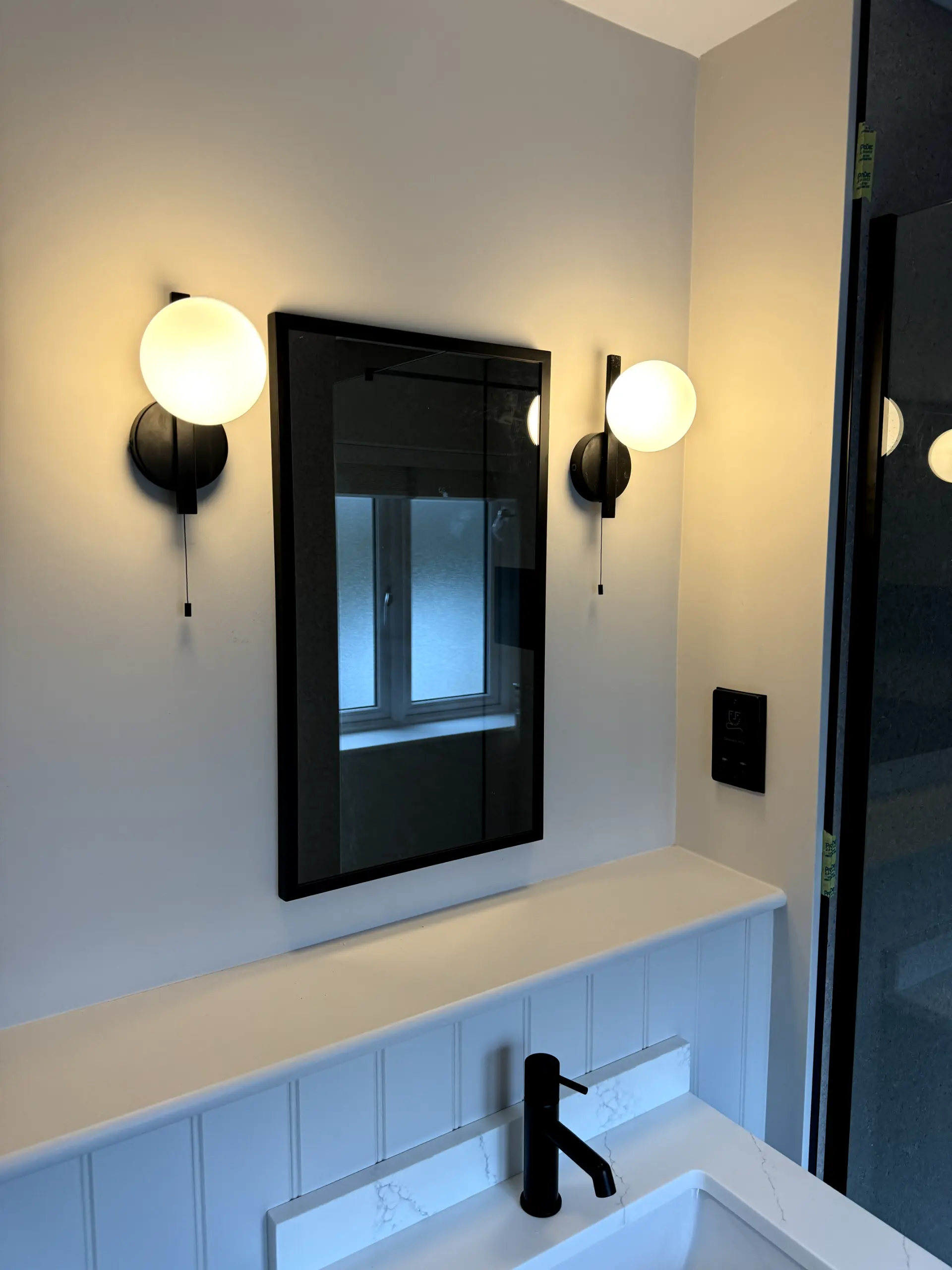 Professional bathroom lighting installation featuring modern globe wall lights next to a mirror
