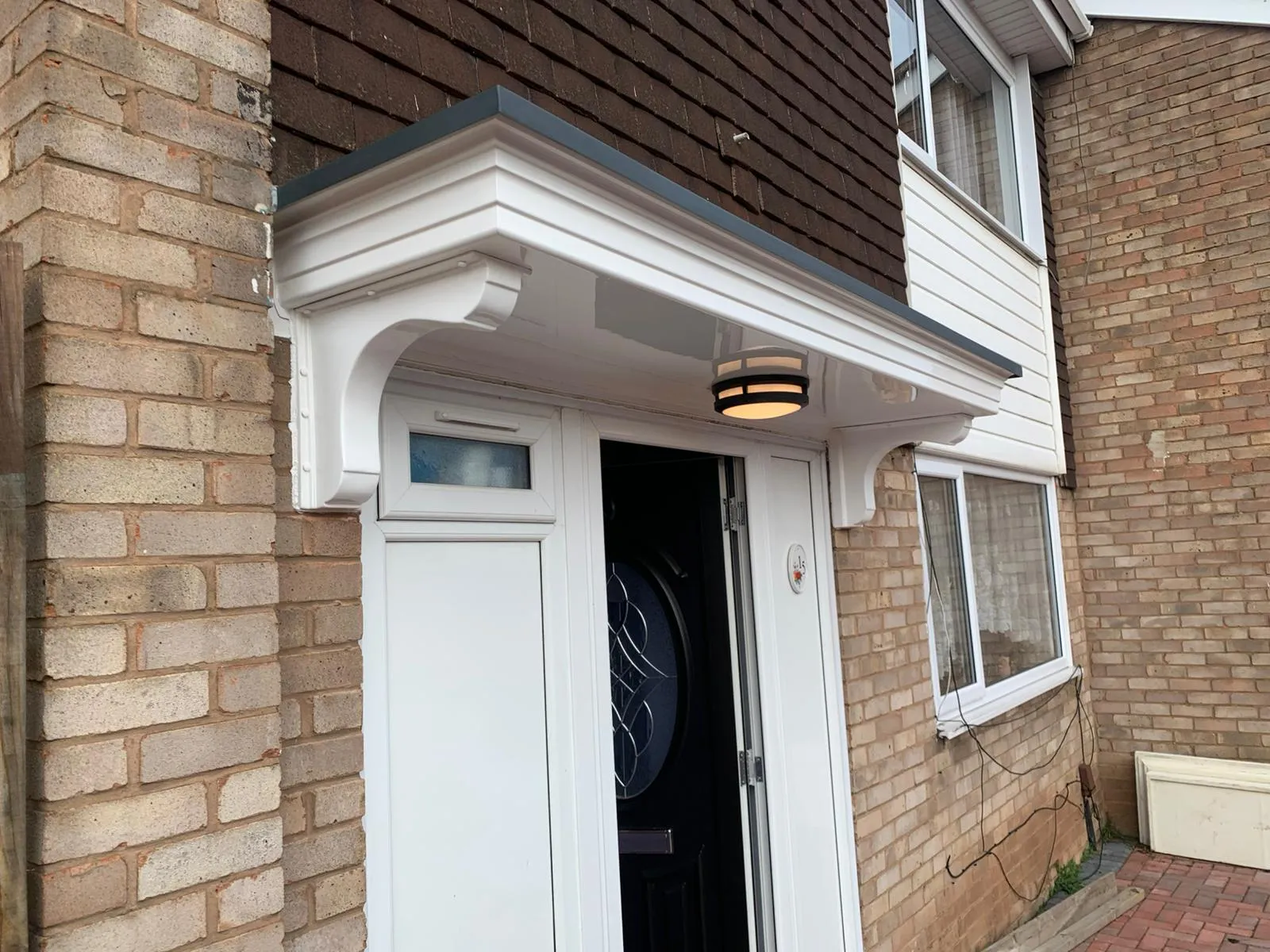 A white uPVC door canopy and roofline installation on a brick house