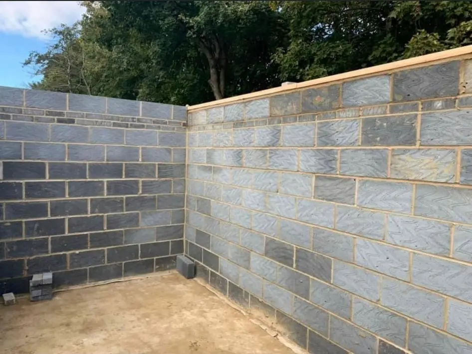 A newly built grey block retaining wall in a garden setting, constructed by Aline Construction.