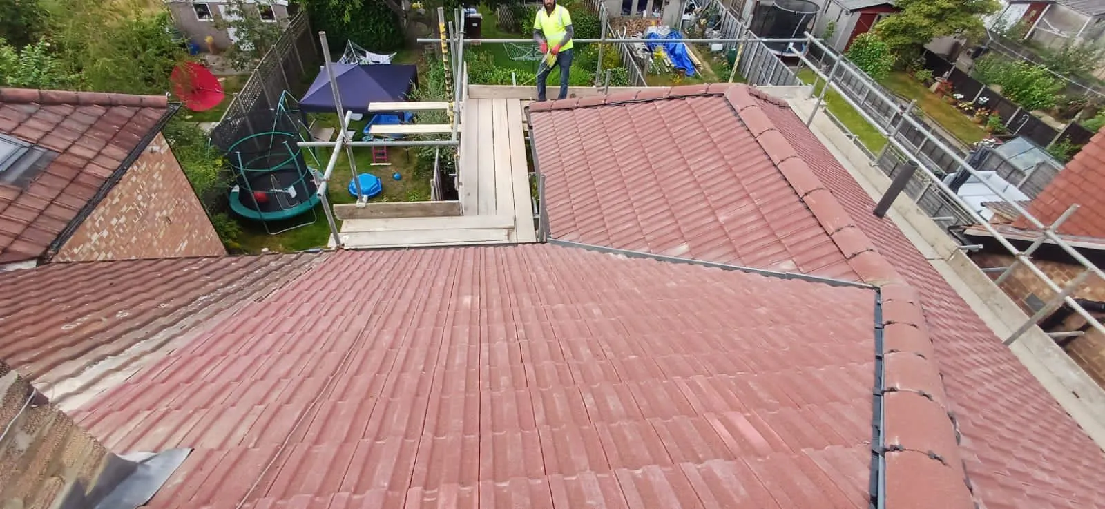 New red concrete tile pitched roof installation with dry ridge detailing and scaffolding on a residential home