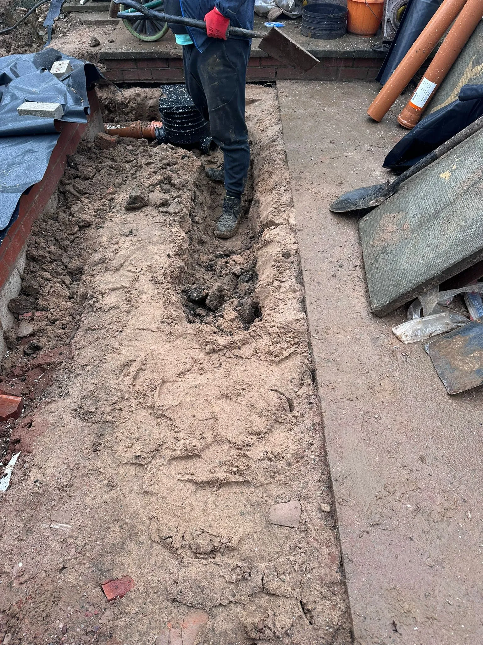 Drainage excavation work in Cheshire showing a trench, new orange pipes, and a black inspection chamber being installed.