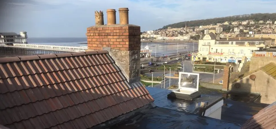 A pitched tiled roof and brick chimney overlooking a coastal town