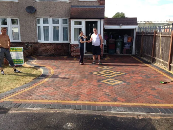Finished block paving driveway with red, black, and yellow blocks in a herringbone pattern and a unique central design, in front of a house, by Elite Paving & Roofing LTD.