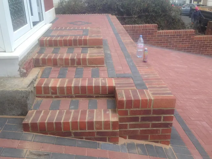 Detailed view of new block paving installation with red and grey bricks, forming steps, a pathway, and a low border wall at a house entrance.