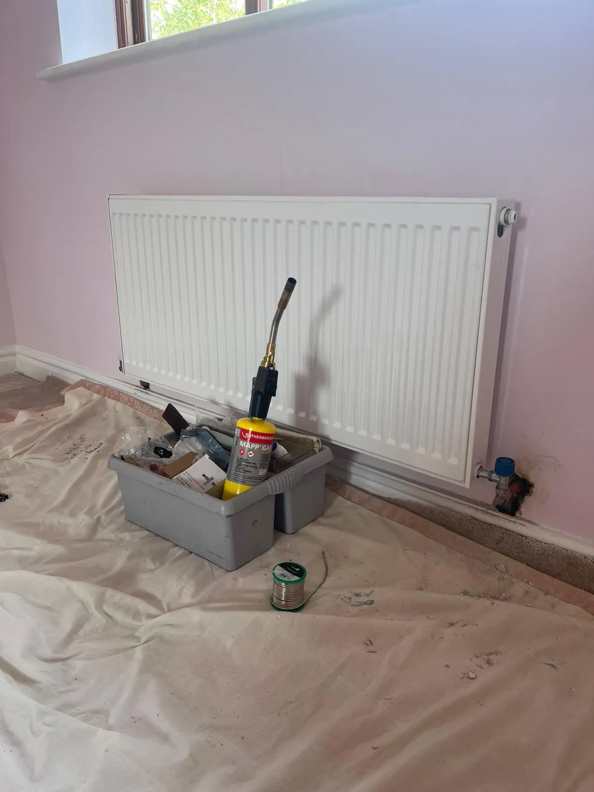 A white radiator being installed on a pink wall by Redorr Heating & Cooling Services Ltd, with a blowtorch and plumbing tools in the foreground.
