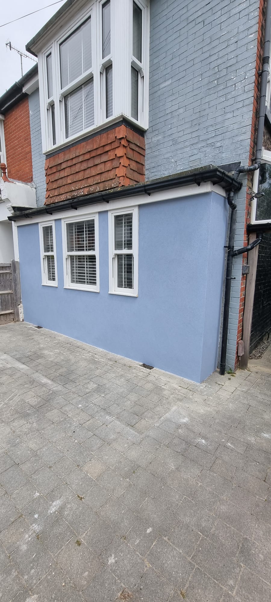 External wall with professional light-blue silicone rendering and white window frames.