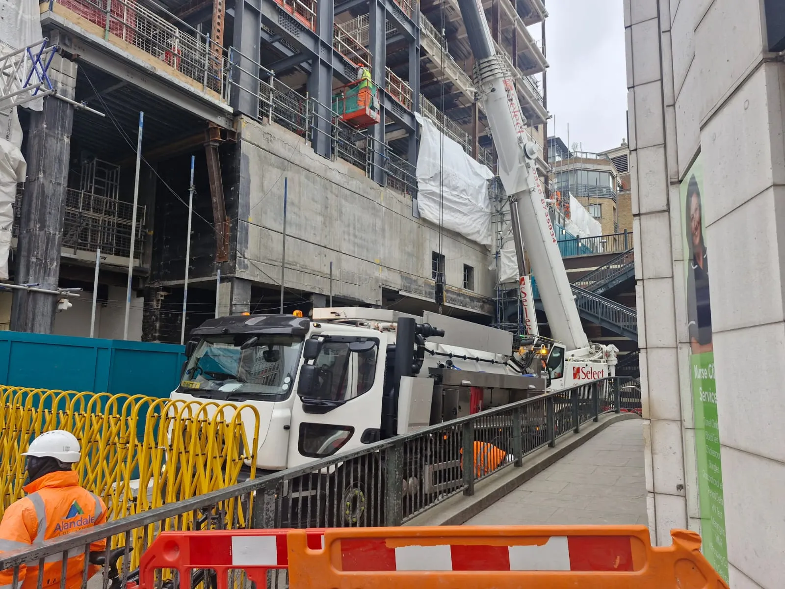 A white vacuum tanker truck and a large mobile crane on a commercial civil engineering site in an urban area.