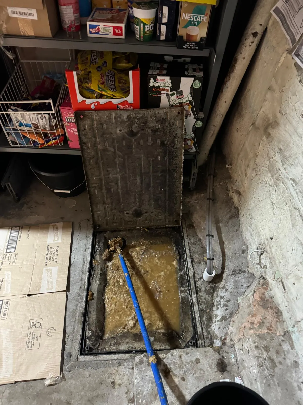 Blocked drain with foul water and debris, being cleared with a drain rod.