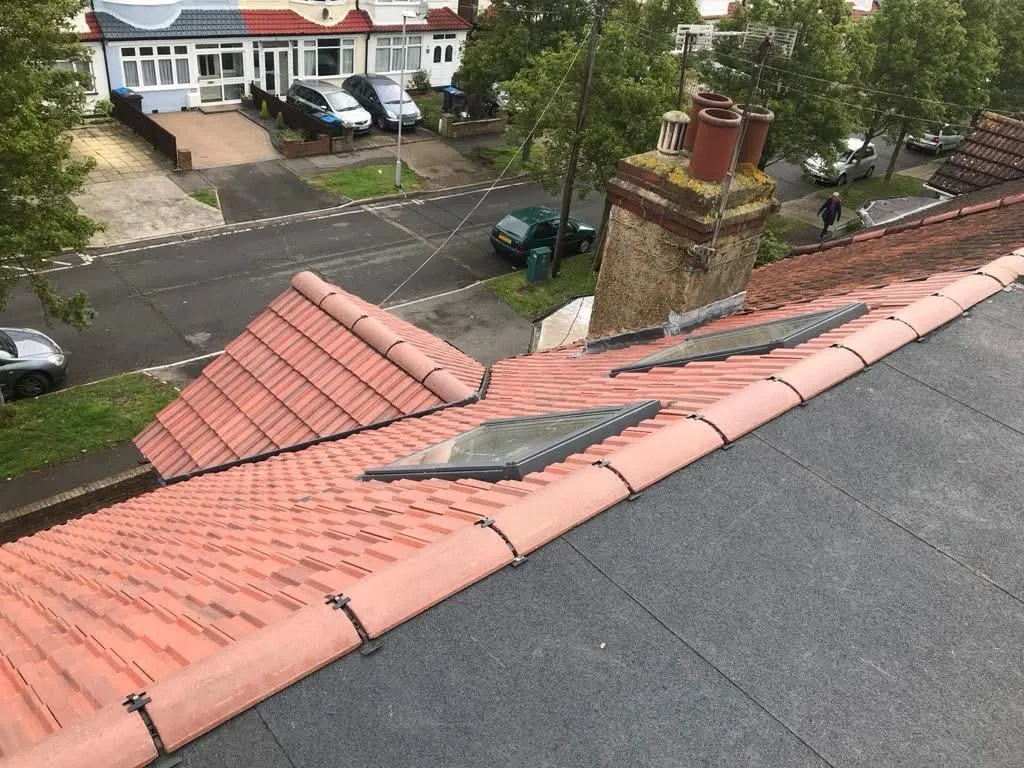 Overview of a residential roof with terracotta tiles, flat roof, skylights, and chimney