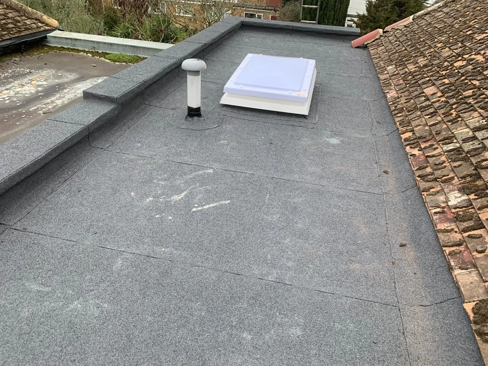 Torch-on felt flat roof installation with integrated skylight and parapet detailing on a residential property