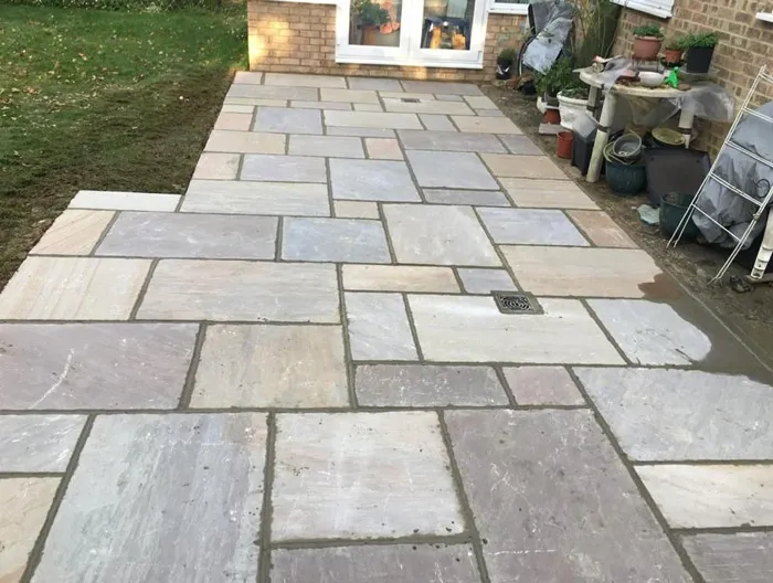 Newly laid Indian Sandstone patio with varied natural stone slabs, a drain, and a freshly edged lawn.